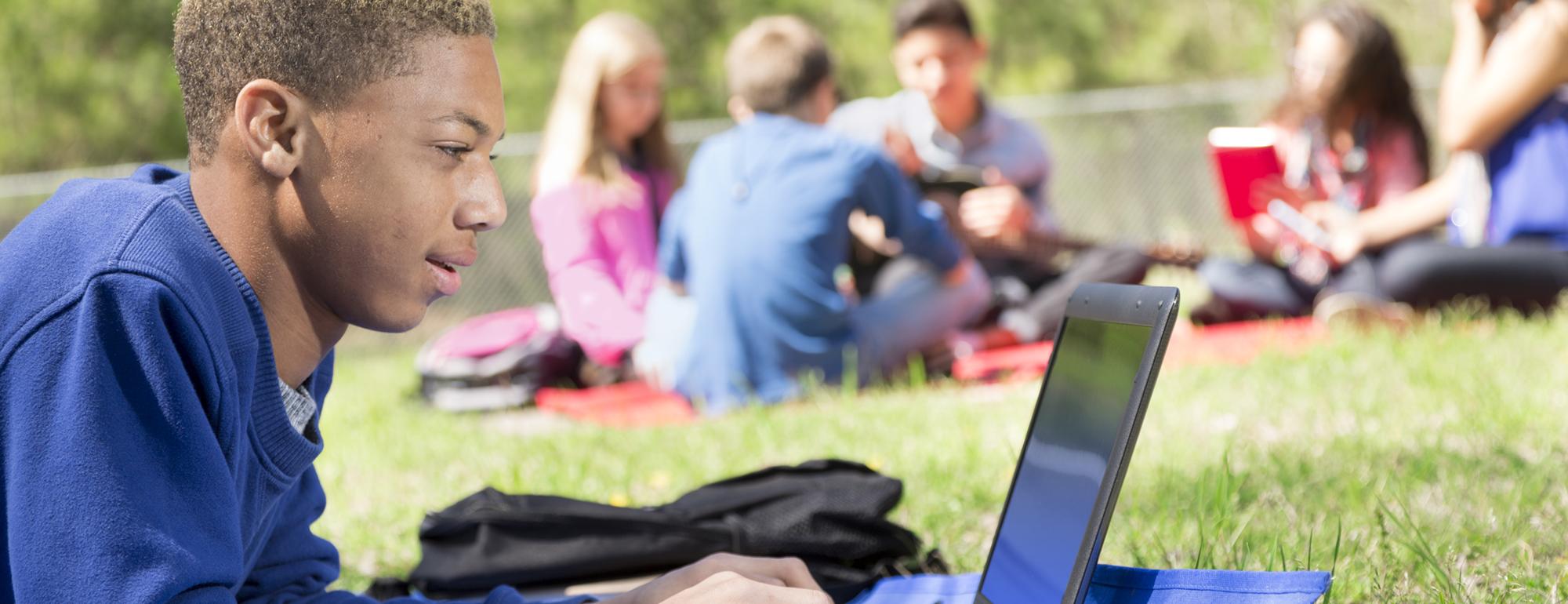teen boy on laptop at park